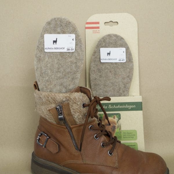 Zwei Schuheinlagen aus Alpakafilz mit einem Schuh im Fordergrund. Eine Schuheinlage steckt im Schuh, die zweite Schuheinlage ist in Karton verpackt.